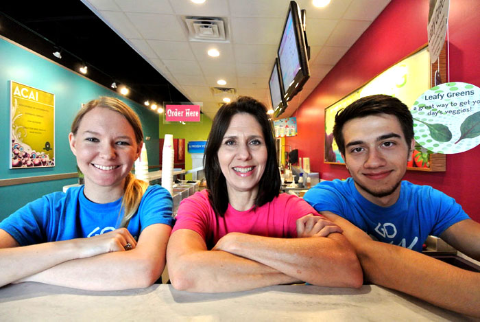 Smiling planet smoothie franchisees in front of a bright red blue and green background