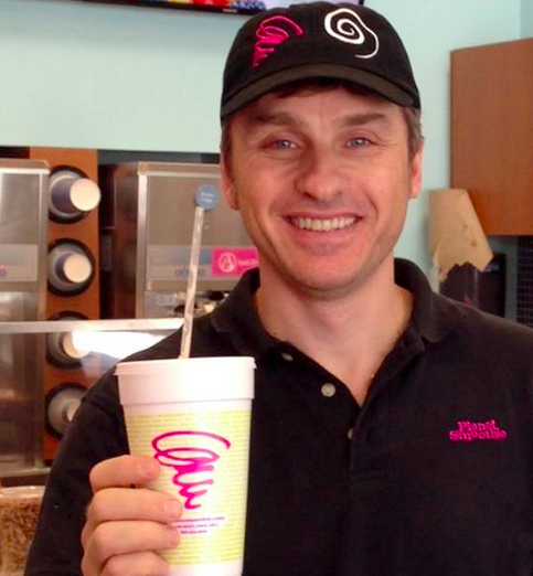 Smiling planet smoothie employee in black and pink planet smoothie uniform drinks a smoothie 