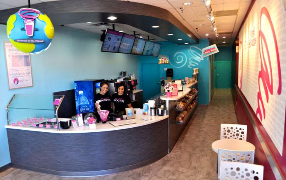 two smiling planet smoothie staffers in the clean well lit interior of planet smoothie which is bright blue and pink 