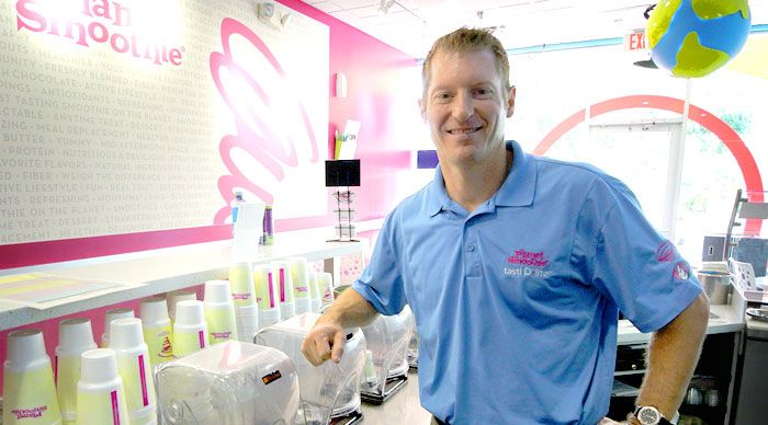 Jason Mann smiles as he makes smoothies in his bright pink Planet Smoothie Franchise