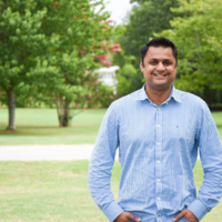 Jimil Patel stands smiling in front of a green background