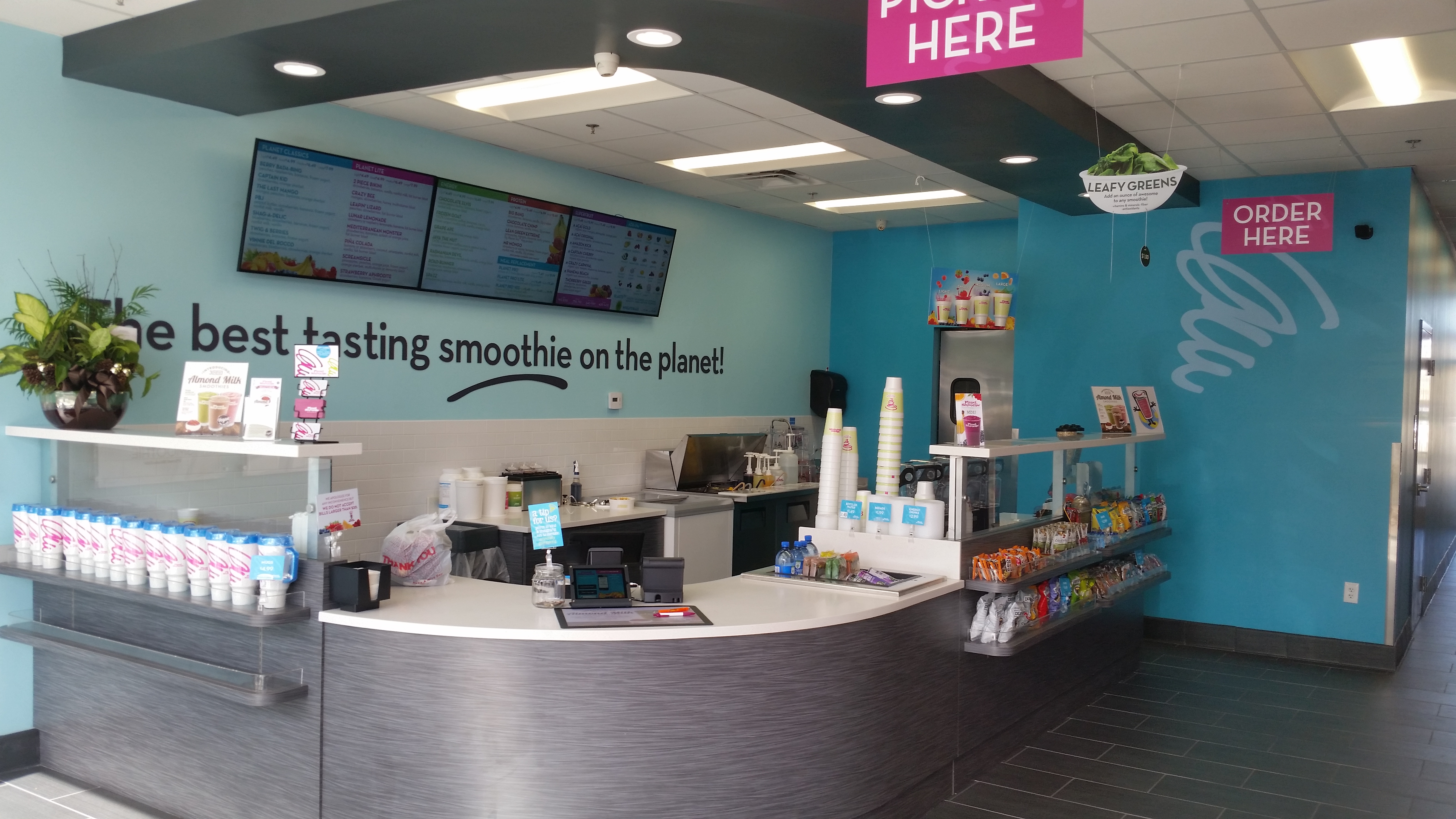 The bright blue interior of a planet smoothie with chrome counters and pink signs / on-trend